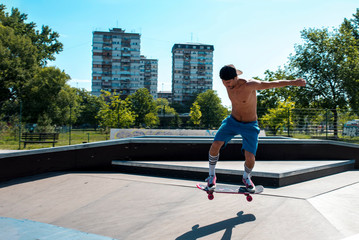 Fototapeta na wymiar Skateboarder practicing at the skate park, jumping over the ramp