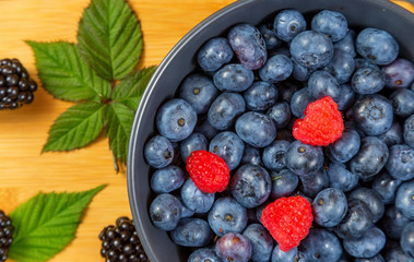 blueberry berry in dark gray ceramic bowl on dark blue wooden background.