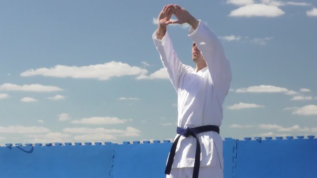 Formal karate exercises performed by an athlete in karategi against a blue sky with clouds