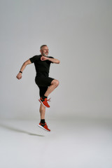 Full length shot of cheerful middle aged muscular man in black sportswear jumping while having...