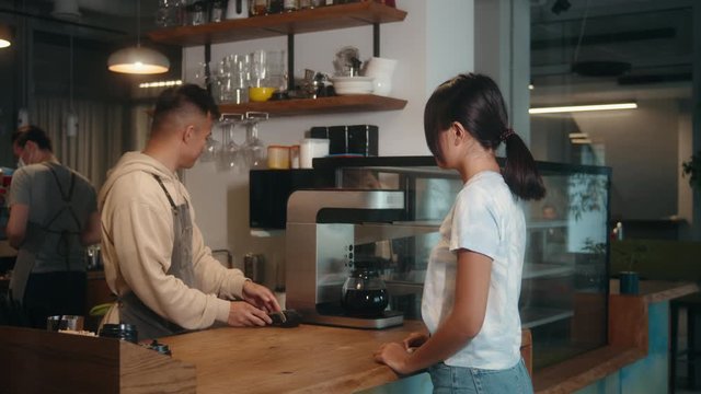 Asian man barista in cafe coffee shop, lockdown, quarantine, coronavirus is over, back to normal concept. Woman girl buy or purchase coffee contactless, banking terminal nfc payment by phone