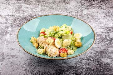 Fresh Caesar salad with grilled chicken, romaine salad leaf, cherry tomato, quail eggs and parmesan cheese on gray background copy space.