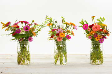 Colorful summer wildflowers in a clear jar on an old wooden table isolated on white with a shallow depth of field