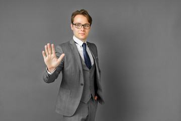 Portrait of a businessman in a suit who stretches out his hand in front of his palm. Stop. Gray background.