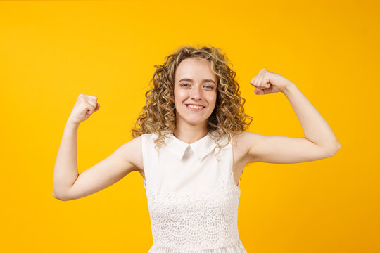 A strong woman with curly hair, a toothy smile, raises her arms and shows her biceps. Look at my muscles