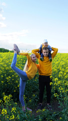 young family with a child in a rapeseed field show the kid how rape grows. family of farmers on a background of yellow flowers in a spring field. family relationships, parenting, love, harmony