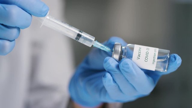Close up shot of unrecognizable nurse or doctor in gloves filling syringe from ampule with covid-19 vaccine