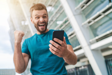 Guy being happy winning a bet in online sport gambling application on his mobile phone
