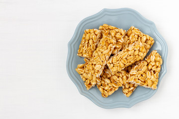 Plate of peanut brittle candy pieces. Top view on a white wooden background.