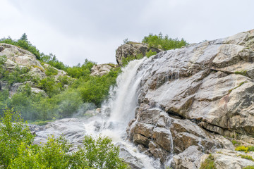 Waterfall on summer day in nature. Rapid water stream falling from rocks against blue sky on sunny summer day in countryside