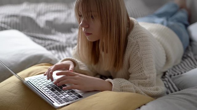 Attractive teen lying in a bed with notebook chatting online