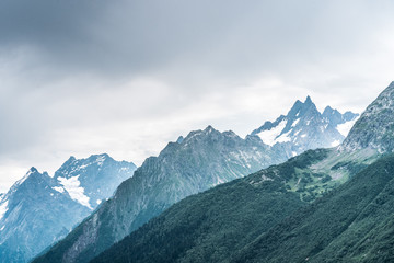 Beautiful mountain landscape in summertime. Mighty mountains with snow in cloudy weather.