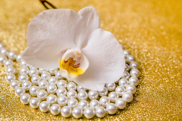 Obraz na płótnie Canvas White Orchid and pearl necklace on a shiny gold background 