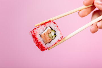 Tasty sushi roll California with wooden chopsticks on pink background close up. Place for caption and text