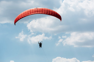 Red Paraglider flying into the sky with clouds on a sunny day