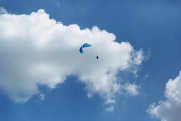 Blue Paraglider tandem instructor with a tourist flying into the sky with clouds on a sunny day