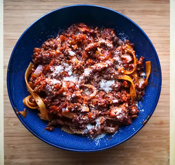 Homemade bolognese pasta topped with parmesan served in a blue ceramic bowl. Coking at home and food backgrounds concept. Flatlay, from above, top view, on the table. 