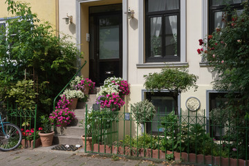 Closeup of the stairs to the entrance door of an old historic building, in the fore different flower pots and a small green garden