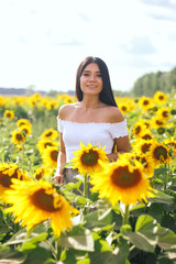 Naklejka na ściany i meble Beautiful brunette woman in a white top on the field with sunflowers. Yellow sunflowers. Close plan.