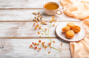 Orange macarons or macaroons cakes with cup of apricot juice on a white wooden background. Side view, copy space.