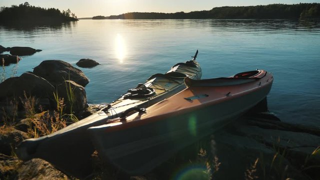 empty small color plastic kayaks stand by rocky bank of large calm lake at picturesque sunset in summer evening close view