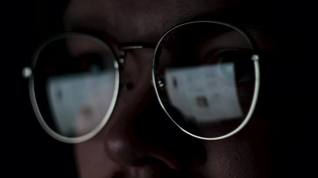 Close up of the eyes of a man with glasses at the computer isolated on black background. Concept. The reflection of the screen in the glasses of a genius or nerd working at night.
