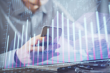Double exposure of man's hands holding and using a phone and financial graph drawing. Analysis concept.