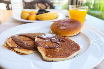 Continental breakfast with pancakes and chocolate served in restaurant. Fruits and orange juice. Morning, outdoor breakfast. Selective focus, close-up