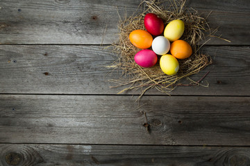 .Painted easter eggs in a makeshift straw nest on a wooden background