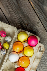 Dyed easter eggs in cardboard box on wooden background.