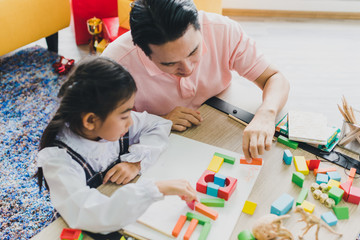 Asian father and daughter play a jigsaw on the table in the words "Love." In the living room decorated with Christmas trees to prepare to celebrate Christmas and New Year.