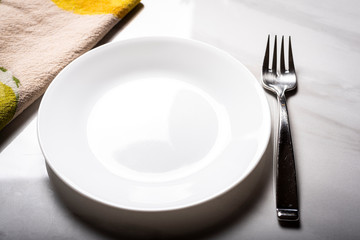 Empty white plate, fork and cloth on a marble surface with shadows