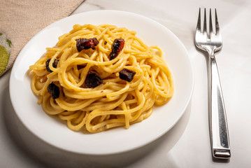 Spaghetti Carbonara on a white plate, fork and cloth on a marble surface with shadows