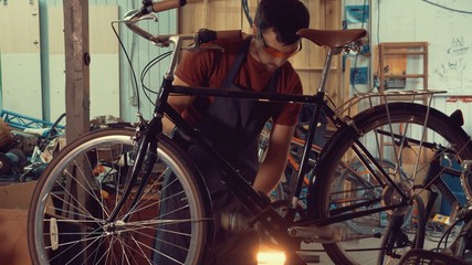 theme small business bike repair. A young Caucasian brunette man wearing safety glasses, gloves and an apron insists the speed switches on the bicycle handlebar in the garage of the workshop