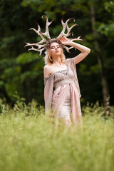 Obraz premium Caucasian Girl With Artistic Deer Horns in Forest. Posing in Light Dress for Demonstrating Forest Nymph Concept. Art Photography.