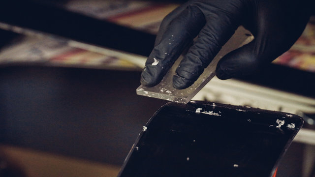 Ski maintenence. Removing excess wax from race ski base plastic scraper. Ski service and repair. Winter shop worker doing base repair. Rental workshop service. Repairman In Workshop Ski Service