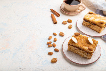 Honey cake with milk cream, caramel, almonds and a cup of coffee on a white concrete background. Side view, copy space.
