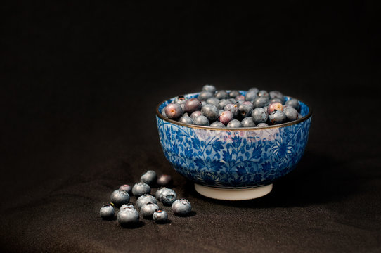 the blue bowl of blueberries over the black background