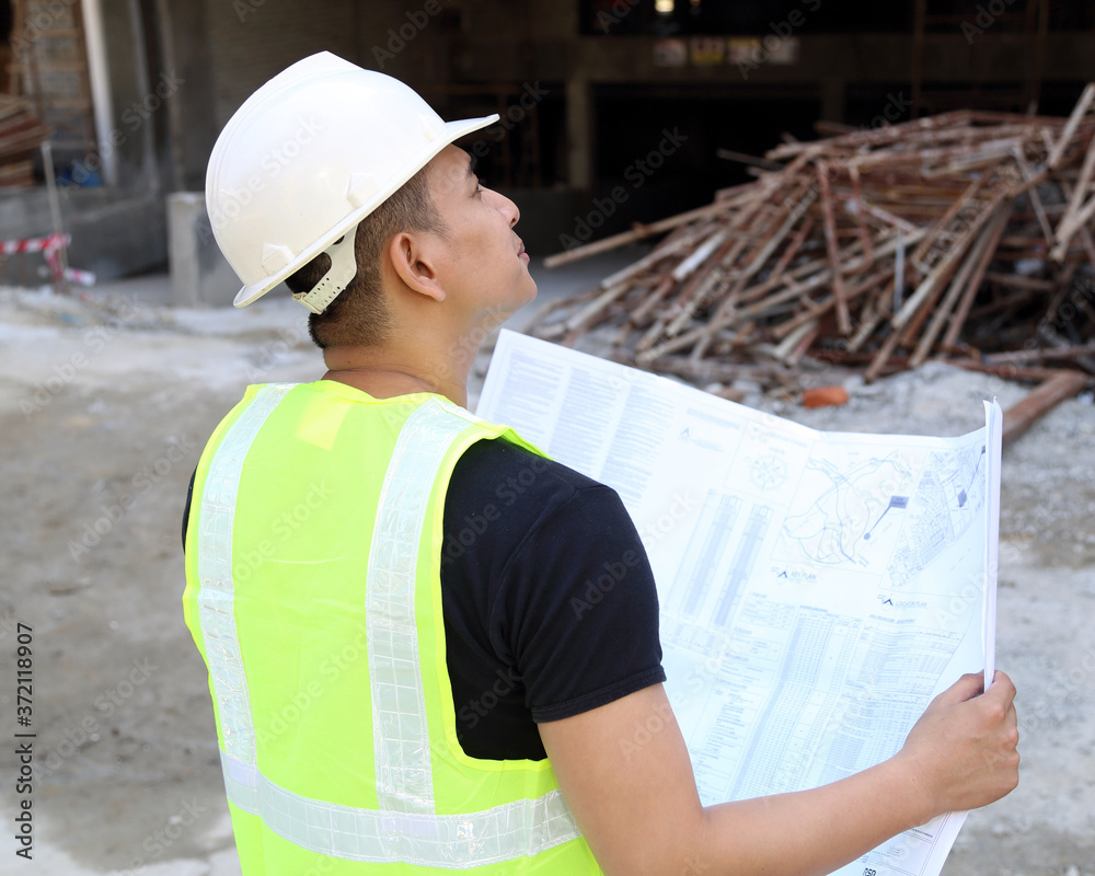 Wall mural south east asian young malay man wearing white safety helmet yellow vest looking carrying blueprint 