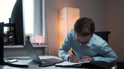 A caucasian businessman working from home with the computer and taking notes on paper
