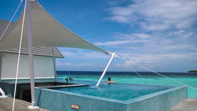 Man alone in swimming pool overlooking sea in beautiful Maldives sunshine