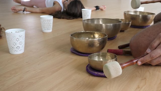 Singing bowls lightly hit with malet on wooden floor with candles and students