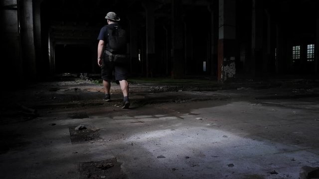 a young man of European appearance in a hat explores the space of the workshop of an abandoned factory. Beautiful reflections and play of light on a dirty gray floor. the shop is not visible