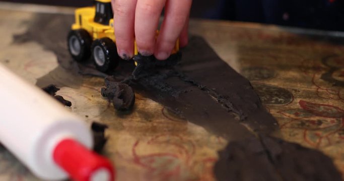 A close-up of a child's hands playing with his tow digger and clay inside during lockdown