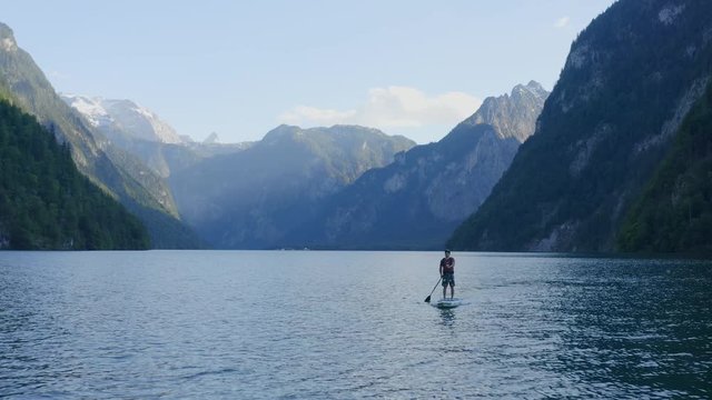 Aerial view moving away shot, Two men on the lake paddle boarding, Scenic view of the mountains and sunlight in the background.