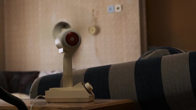 Male hand adjusts the speed of retro fan. Old vintage fan stands on table and blows in the wind. Vintage entourage in the room.