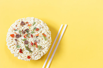 Dry noodles with spices and wooden sticks on yellow background, copy space