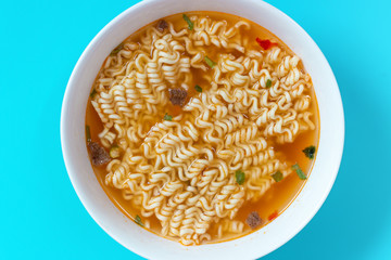 A bowl with ready instant noodles on blue background, top view