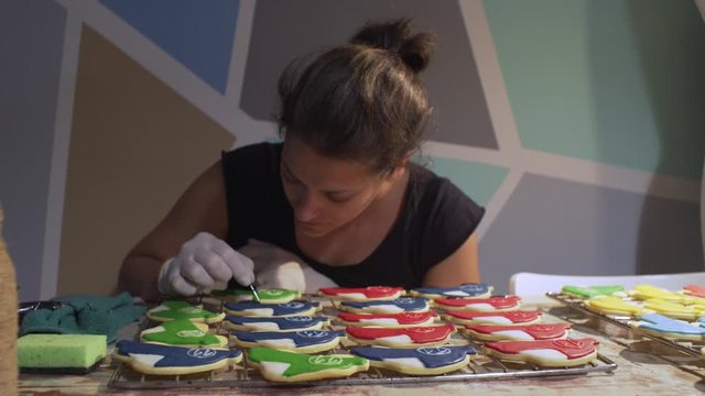 Woman decorates homemade vehicle shaped cookies with sugar icing. Slide shot 4k