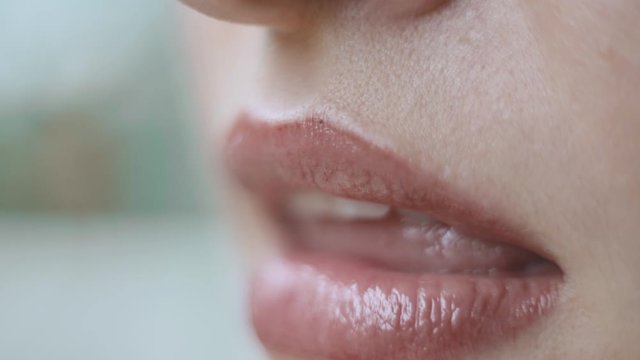 Extremely close up headshot of female face sensually pursing lips with lip gloss. Close up of seductive woman's lips doing a sensual pursing gesture